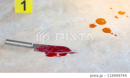 A bloodstained stainless steel knife lying on a concrete floor, with a blurred yellow number 1 sign nearby and blood splatter surrounding the scene, evoking a sense of crime investigation. A bloodstained stainless steel knife lying on a concrete floor, with a blurred yellow number 1 sign nearby and blood splatter surrounding the scene, evoking a sense of crime investigation. 118999744