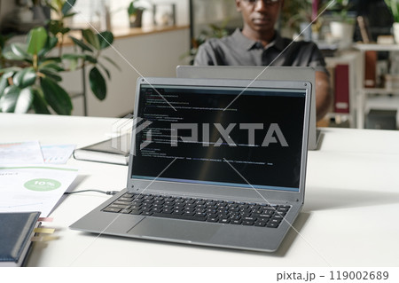 Medium close up of silver laptop with codes on black screen in modern office Medium close up of silver laptop with codes on black screen in modern office 119002689