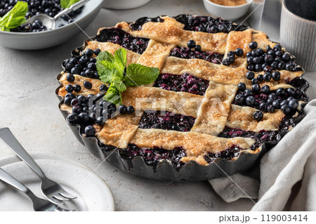 Delicious Homemade Blueberry Pie with mint on gray table with plates and cutlery Delicious Homemade Blueberry Pie with mint on gray table with plates and cutlery 119003414