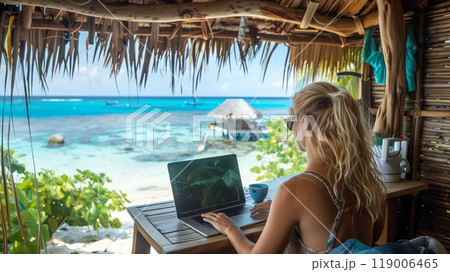A digital nomad entrepreneur works diligently on their laptop in a tropical, beachside cabana. 119006465