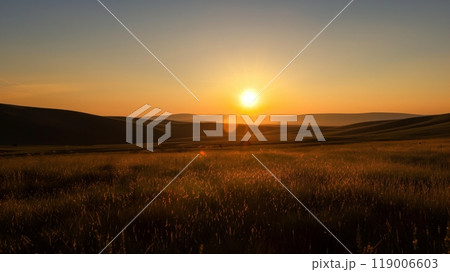 A prairie silhouette stretches to distant hills bathed in the warm hues of a setting sun, casting golden light. 119006603