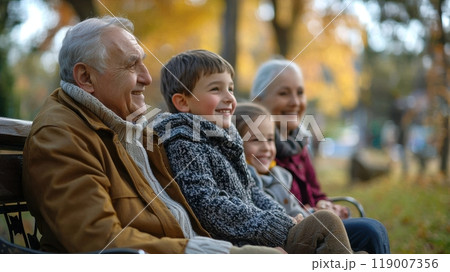 Grandparents watching their grandchildren play in a public park while sitting on a bench, smiling during a peaceful multigenerational family day 119007356