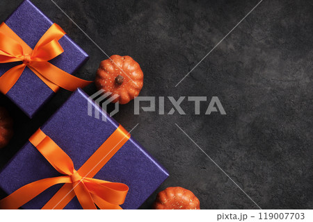 Halloween gifts with purple wrapping paper, orange ribbons, and mini pumpkins on a dark background. Place for your text. Halloween gifts with purple wrapping paper, orange ribbons, and mini pumpkins on a dark background. Place for your text. 119007703