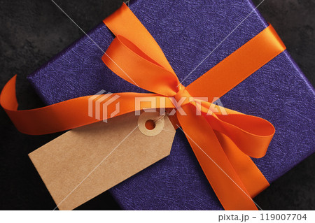 Halloween gift wrapped in purple paper with orange ribbon and rectangular blank tag. A place for your text Halloween gift wrapped in purple paper with orange ribbon and rectangular blank tag. A place for your text 119007704