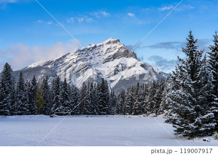Close up snow-covered Cascade Mountain with snowy forest over blue sky and white clouds in winter sunny day. Banff National Park beautiful landscape. Canadian Rockies, Alberta, Canada. 119007917