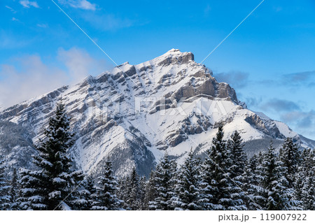 Close up snow-covered Cascade Mountain with snowy forest over blue sky and white clouds in winter sunny day. Banff National Park beautiful landscape. Canadian Rockies, Alberta, Canada. 119007922