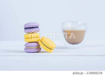 Tasty violet and yellow macarons and cup of latte on white wooden background. 119008238