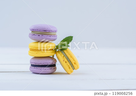 Delicious violet and yellow macarons and green mint leaves on white wooden background. Delicious violet and yellow macarons and green mint leaves on white wooden background. 119008256