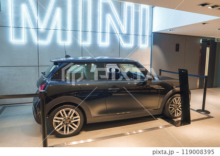 A pristine black Mini Cooper showcased indoors with a large illuminated MINI sign in a high-end dealership or automotive exhibition in London, UK. A pristine black Mini Cooper showcased indoors with a large illuminated MINI sign in a high-end dealership or automotive exhibition in London, UK. 119008395