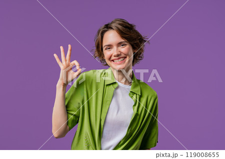 Pretty woman makes hand sign okay, ok gesture. Happy girl, correct perfect choice, great deal, violet background. Positive female model smiles to camera, approval, trust concept. 119008655