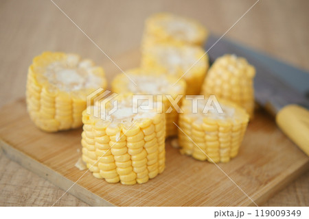 Corn slices on a wooden cutting board with a knife, ready for cooking preparation 119009349
