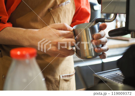 A talented Barista Skillfully Preparing Coffee while Steaming Milk for a Beverage 119009372