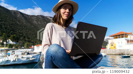 Girl sits with a laptop by the sea on a sunny day. Girl sits with a laptop by the sea on a sunny day. 119009432