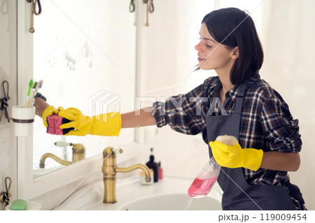 Young woman is washing mirror in the bathrom. 119009454