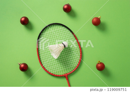 Christmas concept with badminton racket, red balls and white feather badminton shuttlecock on green background. View from above. Xmas greeting card. 119009751