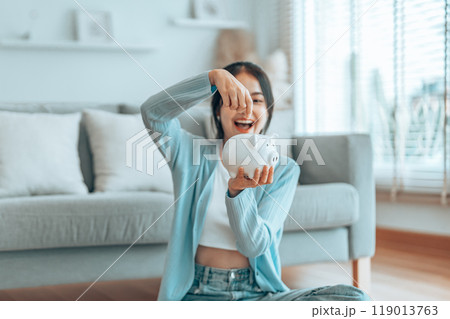 Young Asian woman putting coin in piggy bank. Save money and financial investment Young Asian woman putting coin in piggy bank. Save money and financial investment 119013763