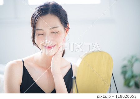 鏡をみながらスキンケアをする肌が美しい素肌感のある女性,目を閉じる 119020055