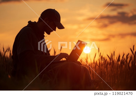 Farmer using laptop in wheat field at sunset, embracing agricultural technology 119021470