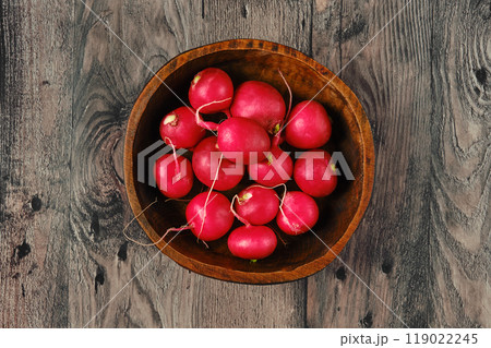 Freshly harvested radishes in a rustic wooden bowl on a weathered wooden surface 119022245