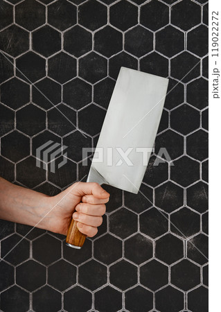 A hand grips a large kitchen cleaver, positioned against a striking hexagonal tile backdrop 119022272