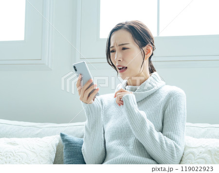 スマホを見ながら悩む女性 スマホを見ながら悩む女性 119022923