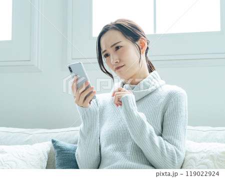 スマホを見ながら悩む女性 119022924