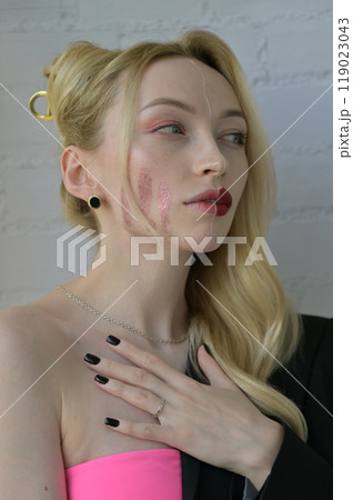Close-up portrait of a blonde girl with different make-up on half of her face and a thoughtful look with hand on the chest on white background Close-up portrait of a blonde girl with different make-up on half of her face and a thoughtful look with hand on the chest on white background 119023043