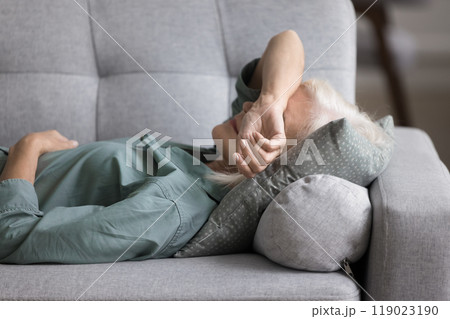 Older woman lying on sofa, feeling fatigued, unmotivated, taking rest 119023190