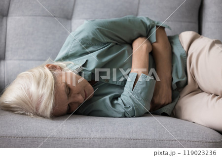 Aged woman clutching her stomach suffers from strong abdominal pain 119023236