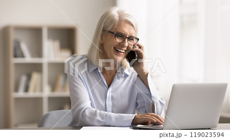 Happy businesswoman typing on laptop keyboard and talking on smartphone 119023594