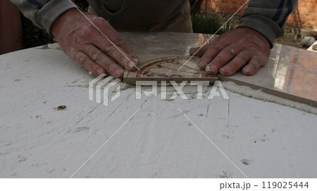 laying decorative ceramic tiles on a table surface to create a tile pattern of geometric pieces, the manual skill of a furniture designer, hands pressing on ceramic material lying on a layer of mortar 119025444
