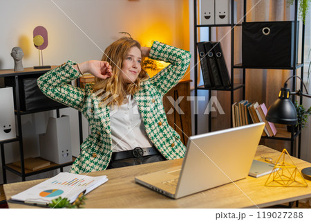 Happy businesswoman at home office desk works on laptop and stretching arms after finishing work 119027288