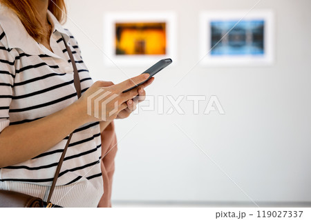 Visitor woman standing takes picture art gallery collection in front framed paintings pictures with mobile phone, Asian female watching at photo frame with smartphone at artwork gallery show Visitor woman standing takes picture art gallery collection in front framed paintings pictures with mobile phone, Asian female watching at photo frame with smartphone at artwork gallery show 119027337