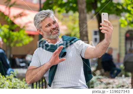 Mature man blogger use smartphone communicating video call online with subscribers recording stories 119027343