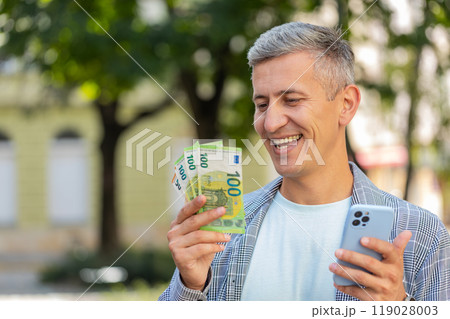 Happy rich man counting holding money euro cash using smartphone calculator app on city street 119028003