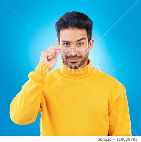 Cool, fashion and portrait of a man with glasses, confidence and winter aesthetic. Sexy style, trendy and a fancy Asian model with fashionable eyewear isolated on a blue background in a studio 119029793