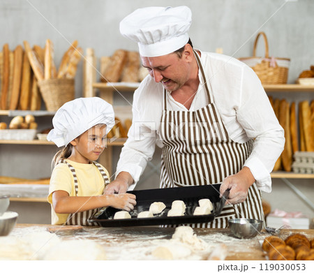 Father and little daughter put raw dough on baking sheet together to make croissants 119030053