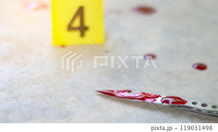A bloodstained stainless steel knife lying on a concrete floor, with a blurred yellow number 4 sign nearby and blood splatter surrounding the scene, evoking a sense of crime investigation. 119031498