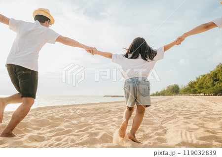 Happy Asian parents with their daughters enjoying playful at beach. Little girls with their mother and father holding hand of child running and pretending on sand. Positive family outdoor activity 119032839