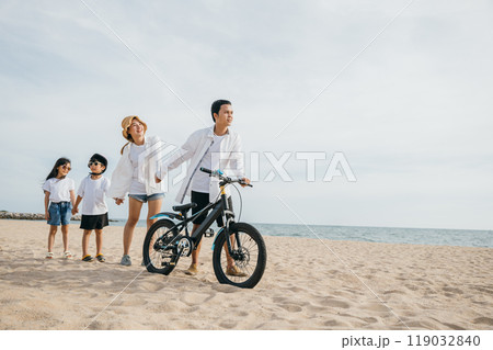 A family on a beach walk parents pushing bicycles a scene filled with happiness smiles and the carefree joy of a childhood day. Family on beach vacation A family on a beach walk parents pushing bicycles a scene filled with happiness smiles and the carefree joy of a childhood day. Family on beach vacation 119032840