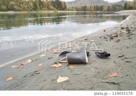 Discarded coffee cup on tranquil lakeshore amidst autumn leaves and scenic Discarded coffee cup on tranquil lakeshore amidst autumn leaves and scenic 119035178