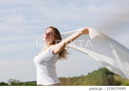 A young woman holds a white cloth in her hands, the concept of purity and freedom A young woman holds a white cloth in her hands, the concept of purity and freedom 119035640