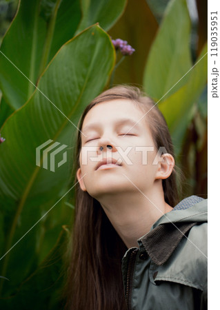 Girl is sitting in a leafy area, wearing a green jacket Girl is sitting in a leafy area, wearing a green jacket 119035951