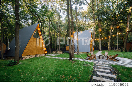 Modern wooden A-frame cabins in forest with outdoor seating and fire pit area, relaxation time 119036091