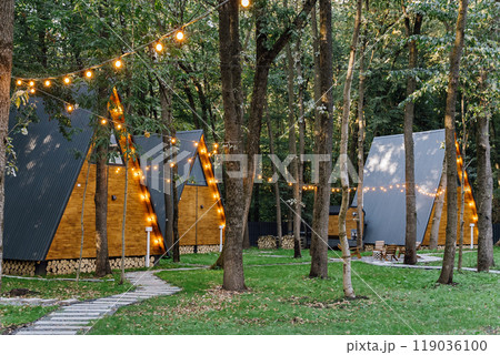 Modern A-frame cabins with glowing string lights in forest environment, ideal for a peaceful retreat 119036100