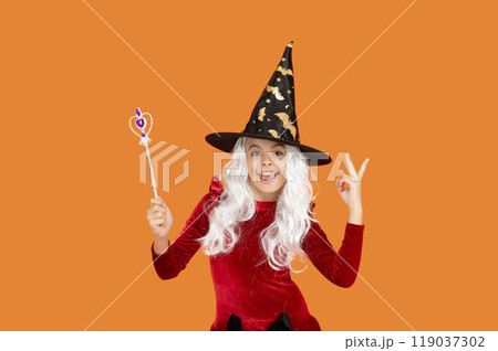 Happy Halloween. Girl witch in Halloween costume isolated on orange. Trick or treat. Halloween costume party. All Hallows witch girl. Girl in witch costume hold magic wand. Peace Happy Halloween. Girl witch in Halloween costume isolated on orange. Trick or treat. Halloween costume party. All Hallows witch girl. Girl in witch costume hold magic wand. Peace 119037302