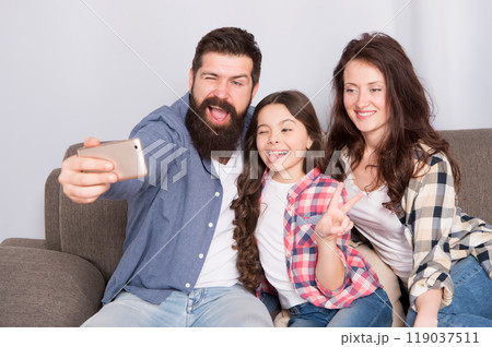 Selfie. Happy family at home. Modern smartphone. Little girl use smartphone with mother and father. bearded man and woman with daughter. Selfie mania. Family make selfie on smartphone. Capturing fun Selfie. Happy family at home. Modern smartphone. Little girl use smartphone with mother and father. bearded man and woman with daughter. Selfie mania. Family make selfie on smartphone. Capturing fun 119037511