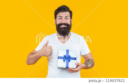 birthday man holding present box. thumb up. bearded man with present box in studio. 119037622