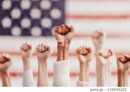 Hands with raised fists show solidarity and unity in front of a blurred American flag, symbolizing strength, activism, and diversity. Hands with raised fists show solidarity and unity in front of a blurred American flag, symbolizing strength, activism, and diversity. 119038202
