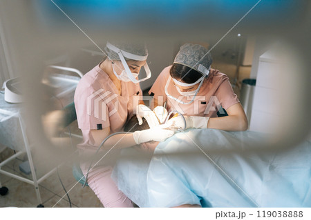 High-angle view of two trichologist specialist collecting hair follicles from back of head of male patient for hair transplantation in clinic. Process of hair transplant with FUE Sapphire method. 119038888
